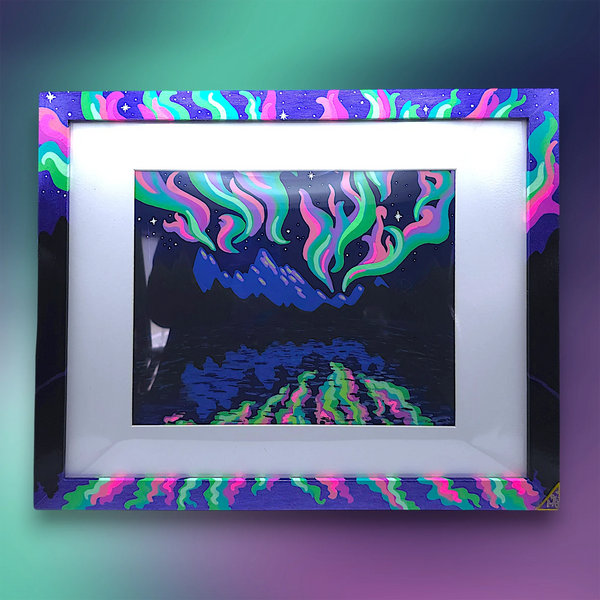 Original northern lights landscape painting titled Aurora Borealis on reflective deep blue foil cardstock in a hand-decorated frame.