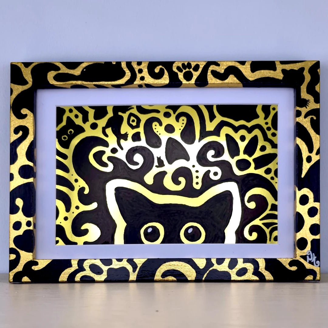 A framed art print featuring a black cat silhouette surrounded by intricate gold and white abstract swirl patterns on a black background, set in a white mat and a black frame with gold cat motifs.