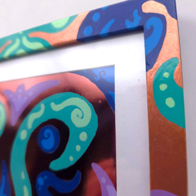 Close-up of a colorful abstract framed artwork with swirling teal, blue, orange, purple, and black patterns, shown against a light neutral background.